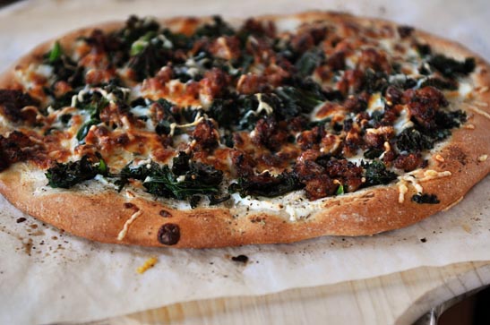 A cooked spinach and bacon pizza on a piece of parchment paper.