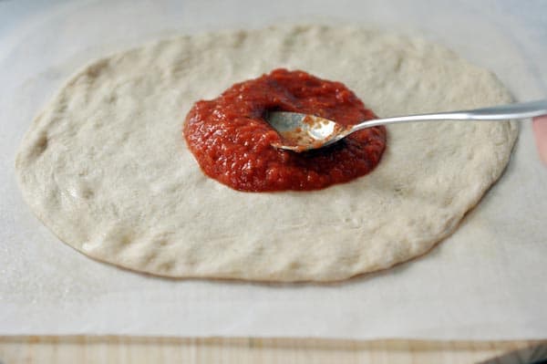 An uncooked pizza crust with red sauce being spread on top. 