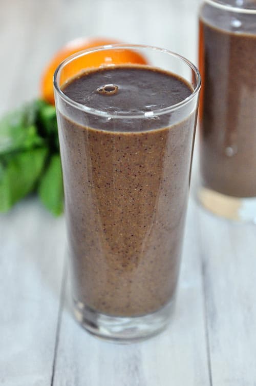 A tall glass cup full of a fruit and vegetable smoothie.