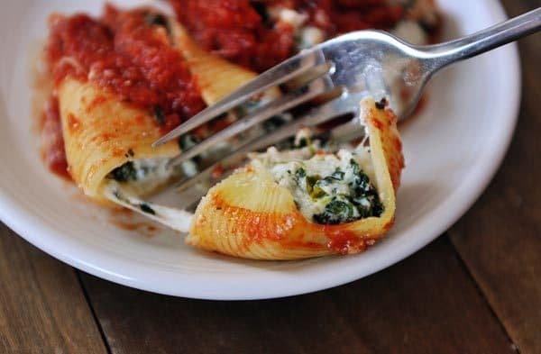 Cheese and spinach stuffed jumbo pasta shells on a white plate. A fork is cutting one in half. 