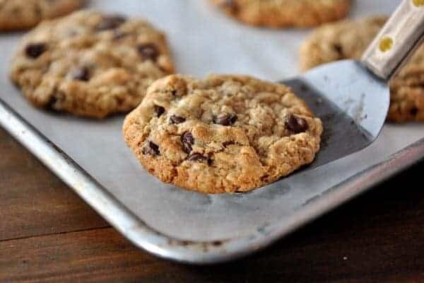 A metal spatula taking a chocolate chip cookie off of a cookie sheet with other baked cookies.