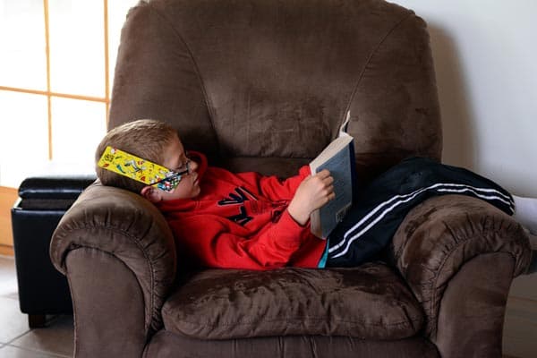 A little boy sitting on a brown recliner reading. 