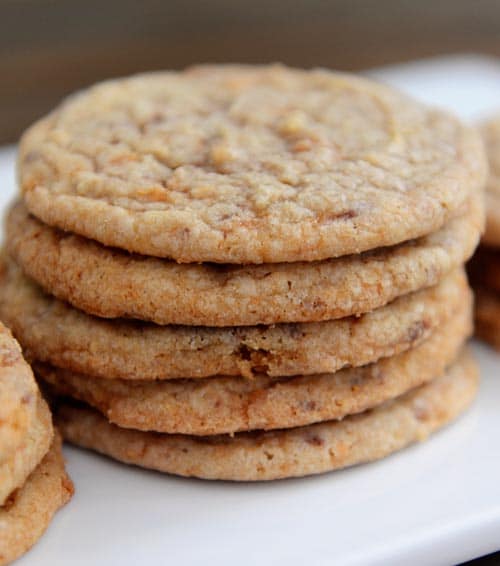 A stack of thin butterfinger cookies on a white plate.