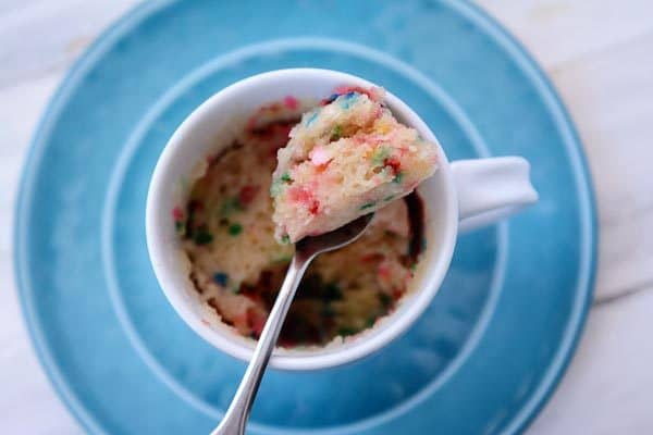 Top view of a spoon taking a bite out of a vanilla funfetti mug cake.