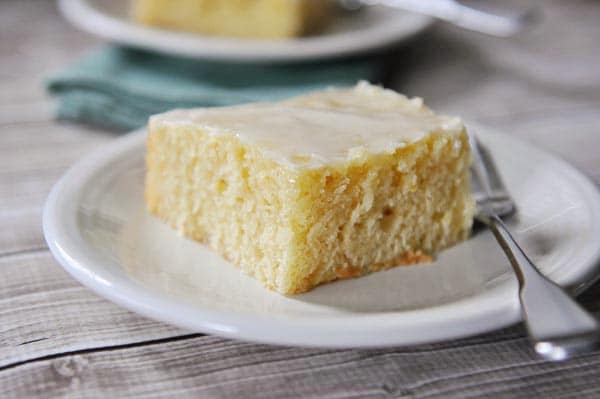 A square piece of glazed lemon sheet cake on a white plate.