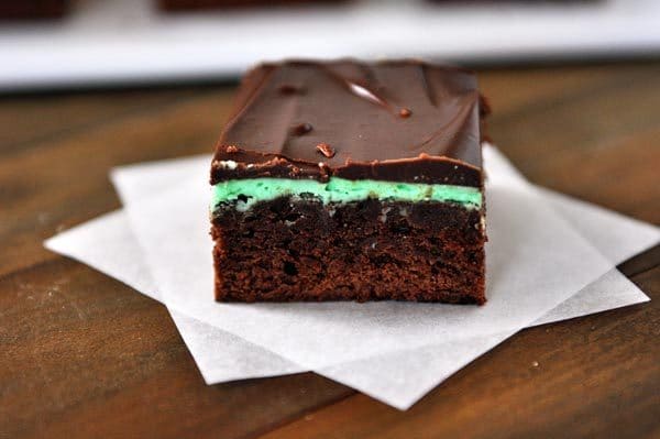 A brownie with layers of mint and chocolate ganache sitting on two squares of parchment paper. 