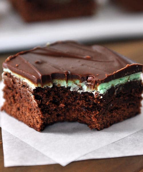 A chocolate frosted mint brownie with a bite taken out sitting on a square piece of parchment. 
