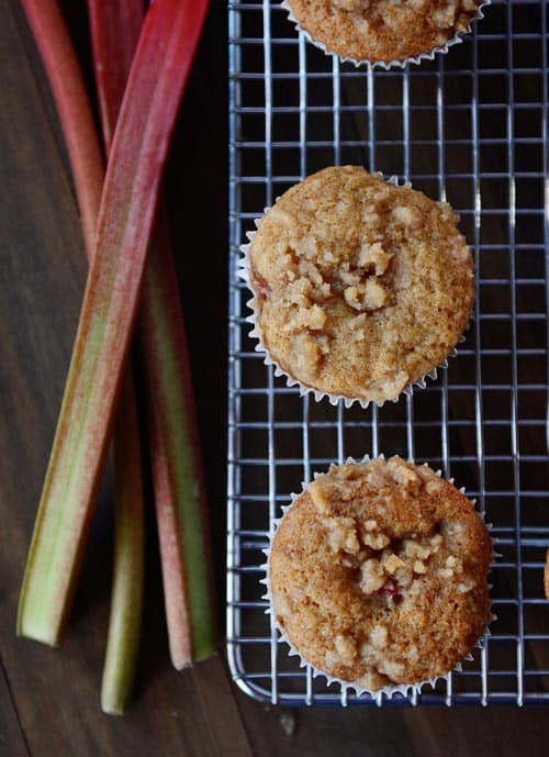 Top view of streusel-topped rhubarb muffins on a metal cooling rack. Fresh rhubarb stalks are on the side. 