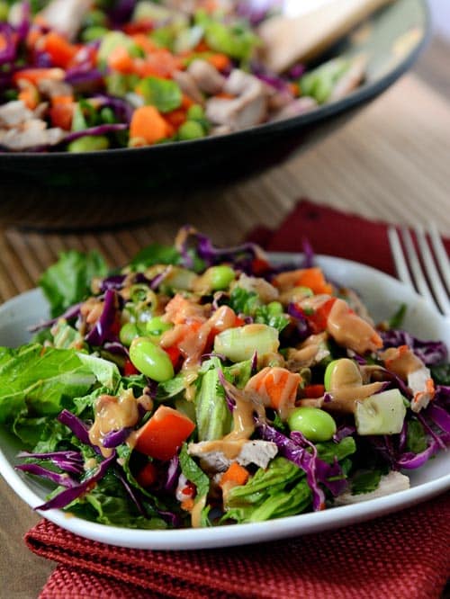 A white plate with a crunchy colorful chopped Thai salad in front of a big bowl of more salad. 