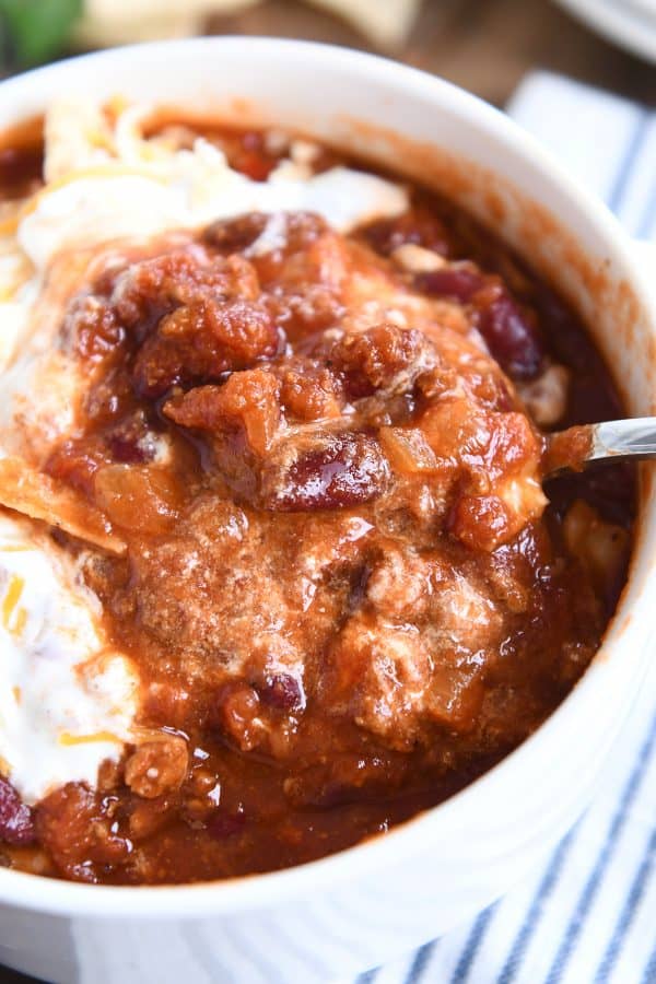 Taking a spoonful of classic slow cooker chili out of a white bowl.