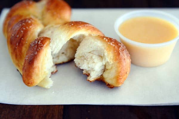 A braided pretzel twist with a chunk taken out next to cheese sauce.