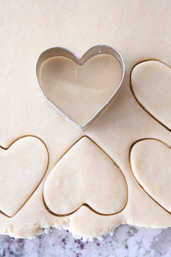 Cutting out sugar cookie dough with heart cookie cutter.