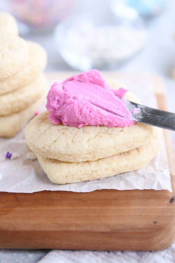 Spreading pink frosting on soft sour cream sugar cookie.