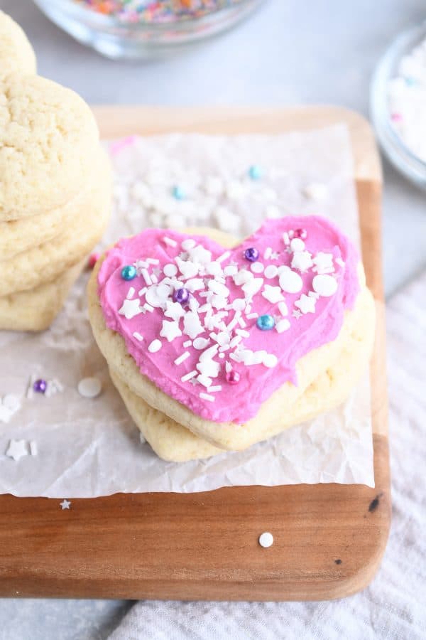 Two sugar cookies with pink frosting and white sprinkles on parchment paper.