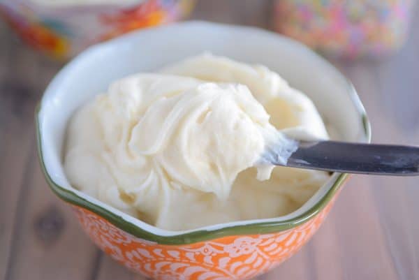 Vanilla buttercream frosting in orange bowl with a metal spatula.