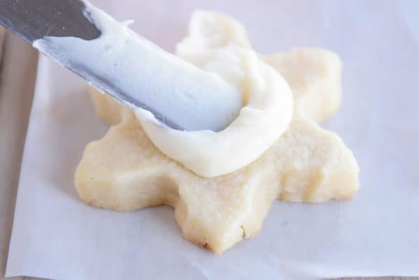 A metal spatula spreading buttercream frosting on a star-shaped sugar cookie.