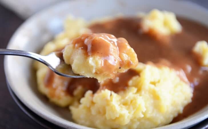 Bowl with mashed potatoes, gravy and spoon.