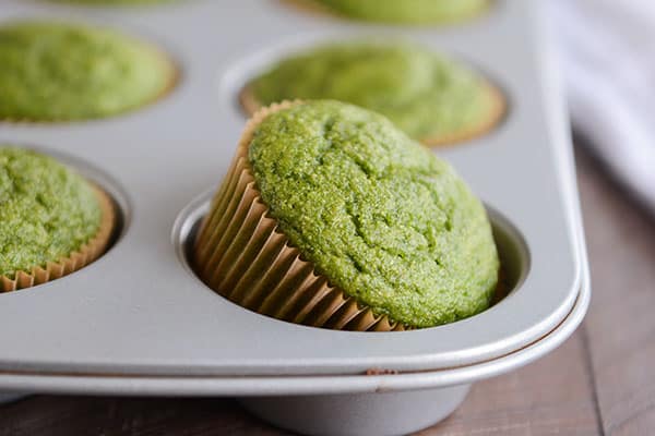 One green muffin in brown liner tipped halfway in muffin tin.