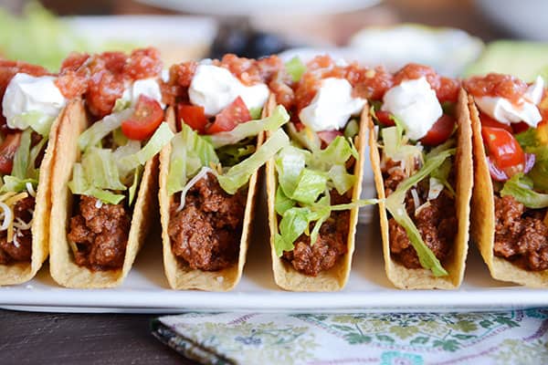 a white plate with filled ground beef tacos lined up next to each other