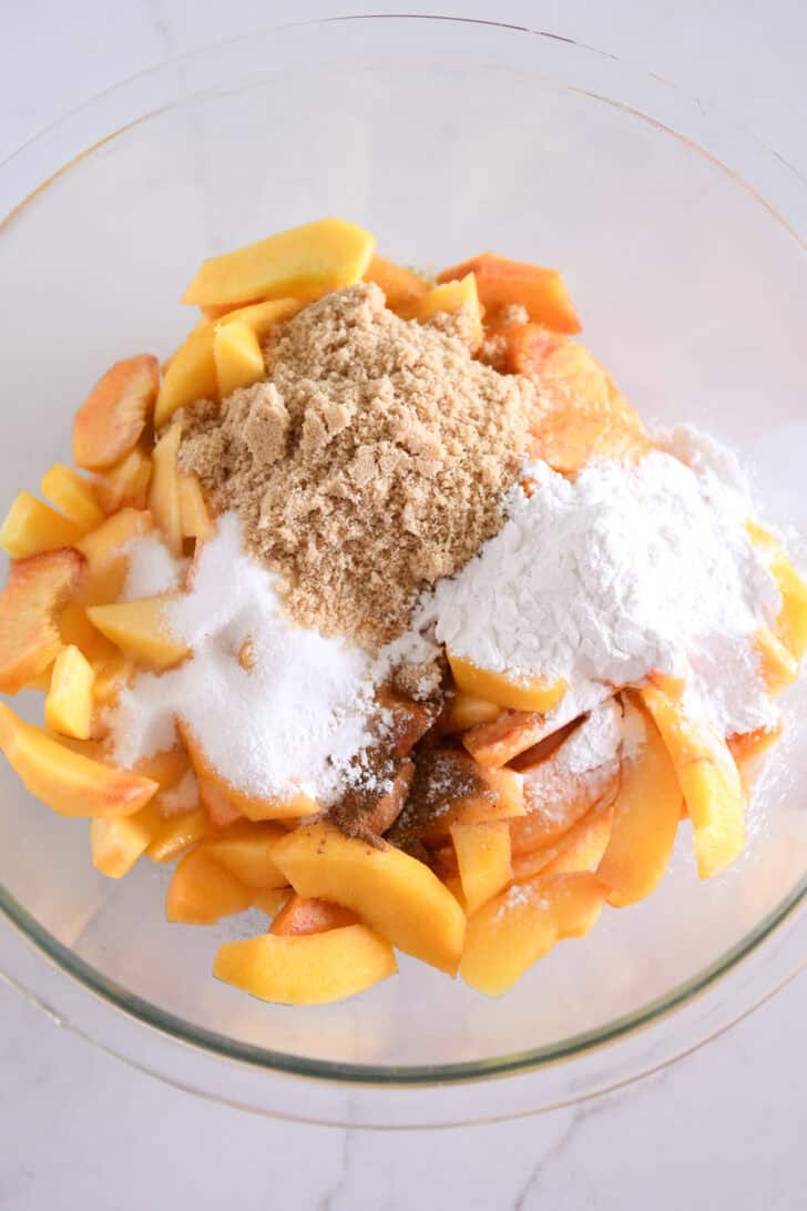 Glass bowl with fresh peaches, brown sugar, granulated sugar, tapioca flour, cinnamon and nutmeg.
