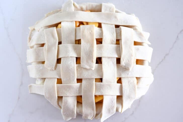 Assembling lattice pie crust on fresh peach pie.