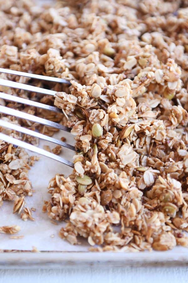 Sheet pan with parchment and spatula sliding granola into a pile.