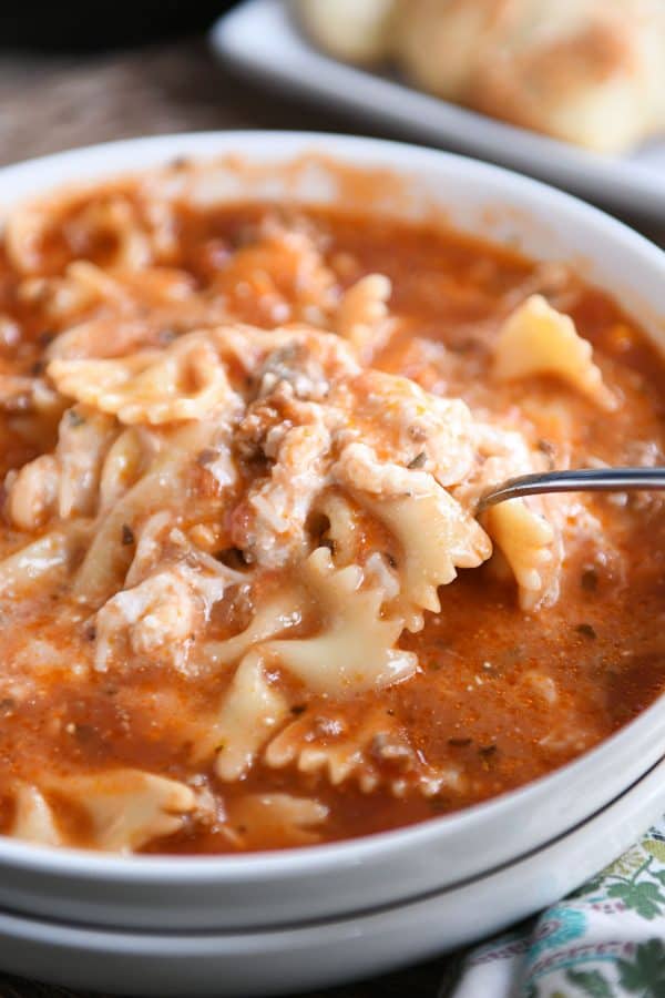 White bowl filled with pressure cooker lasagna soup and spoon taking a bite.