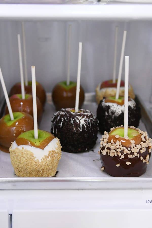 Dipped and decorated homemade caramel apples on sheet pan in refrigerator.