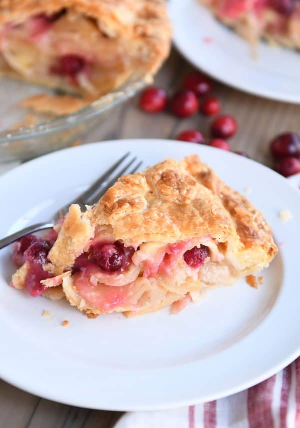 Slice of apple cranberry pie on white plate.