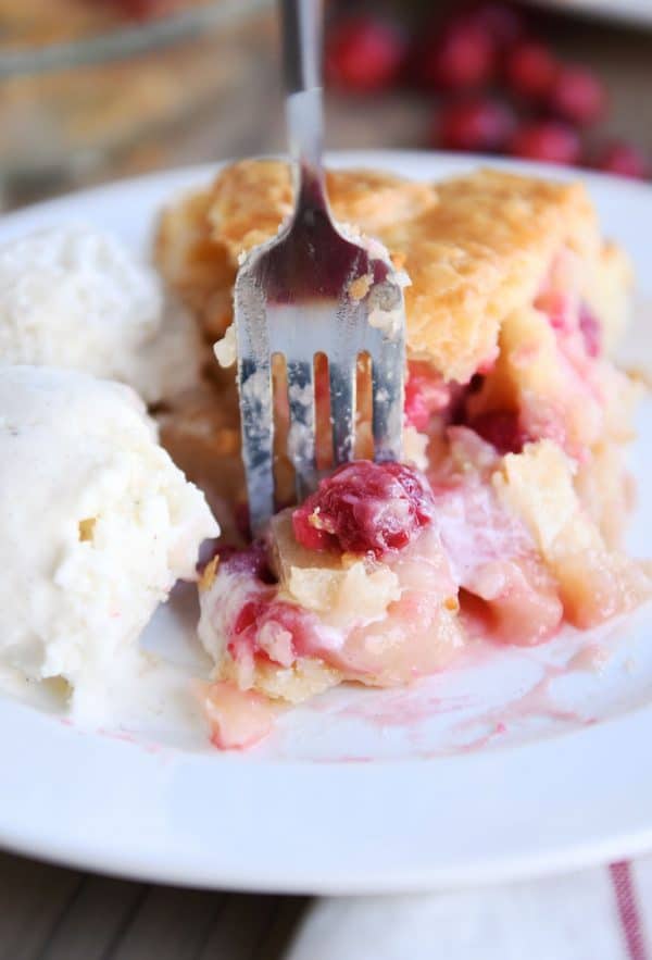 Slice of apple cranberry pie on white plate with ice cream.