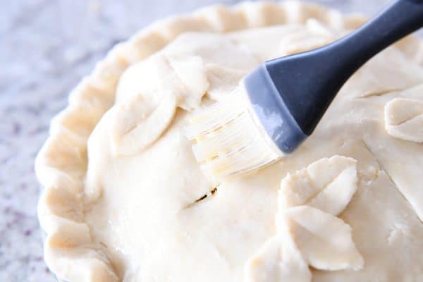 Brushing egg wash on top of apple cranberry pie.