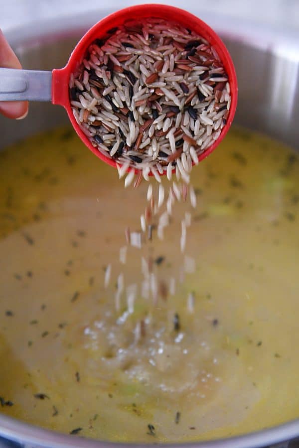 Adding brown and wild rice to pot of creamy turkey soup.
