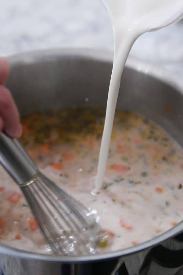 Pouring milk mixture into pot of soup.