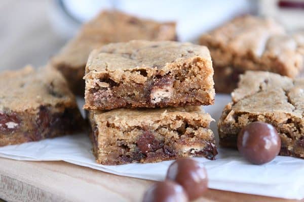 Two malted chocolate chip blondies stacked on white parchment paper.