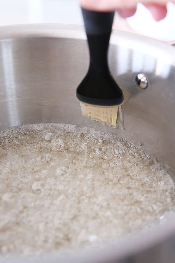 Brushing down the sides of a pot with pastry brush dipped in water.