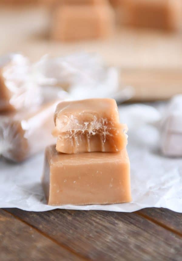 Soft and chewy caramels - two stacked on one another on parchment paper with bite taken out of top caramel.
