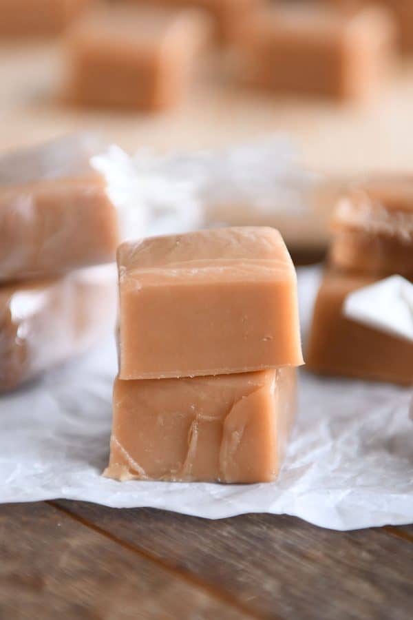 Soft and chewy caramels stacked on one another on parchment paper.