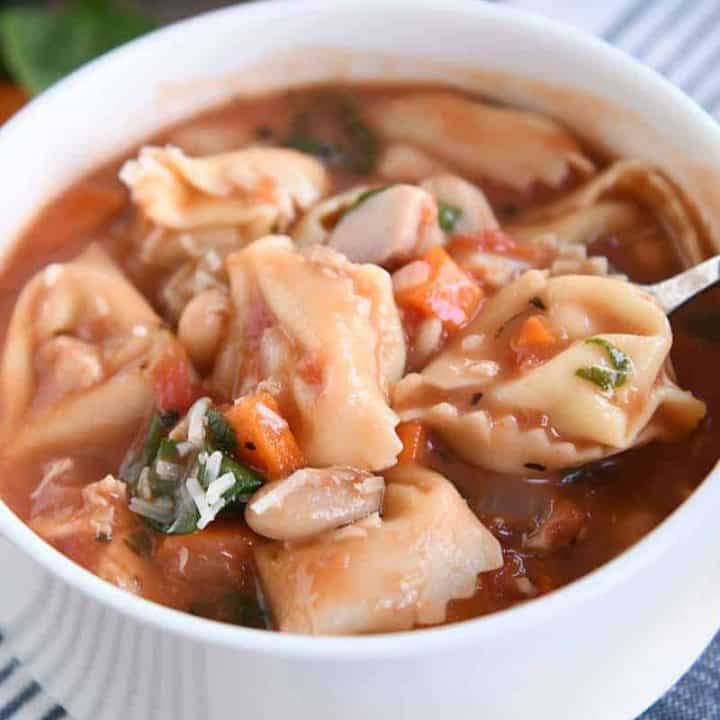 White bowl with handles filled with quick and easy creamy tuscan tortellini soup.