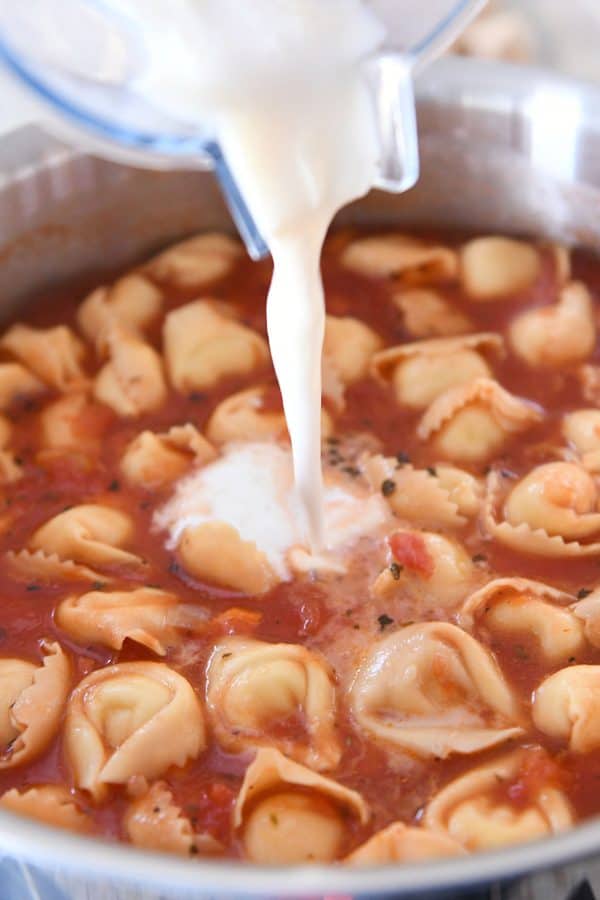 Pouring in milk + flour mixture to quick and easy creamy tuscan tortellini soup.