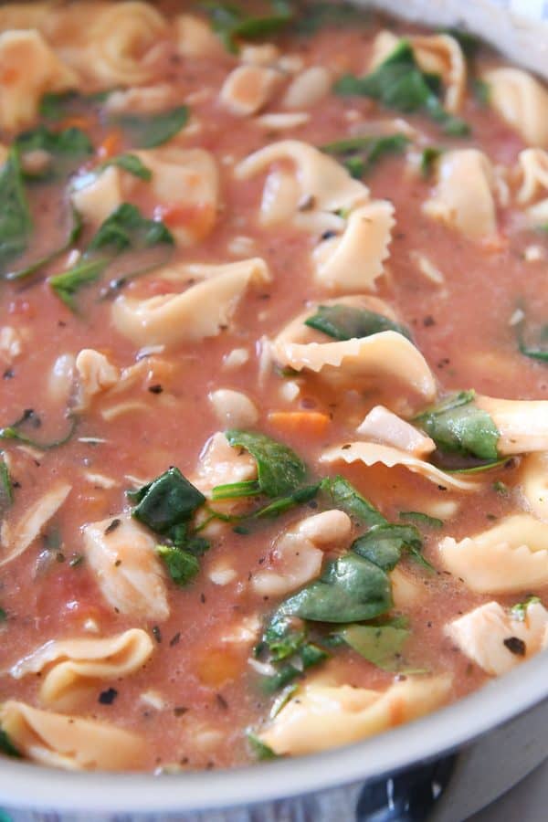Quick and easy creamy tuscan tortellini soup heating in pot on stove.