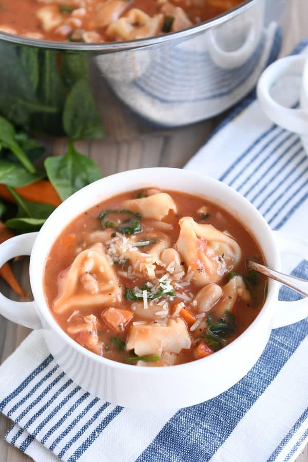 White bowl with handles filled with quick and easy creamy tuscan tortellini soup.