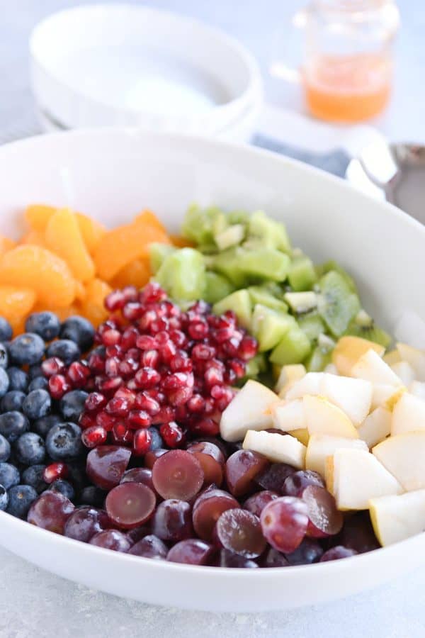 White bowl with grapes, blueberries, pears, kiwi, oranges and pomegranate seeds for easy winter fresh fruit salad.