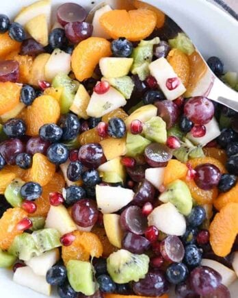 Top down view of white bowl with grapes, blueberries, pears, kiwi, oranges and pomegranate seeds for easy winter fresh fruit salad.