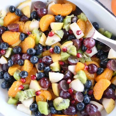 Top down view of white bowl with grapes, blueberries, pears, kiwi, oranges and pomegranate seeds for easy winter fresh fruit salad.