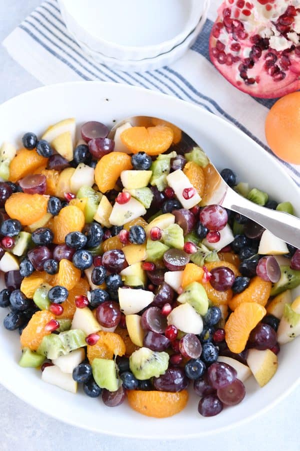 Top down view of white bowl with grapes, blueberries, pears, kiwi, oranges and pomegranate seeds for easy winter fresh fruit salad.