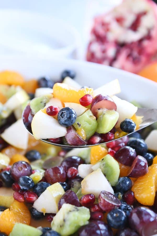 Spoon scooping out winter fresh fruit salad in white bowl.