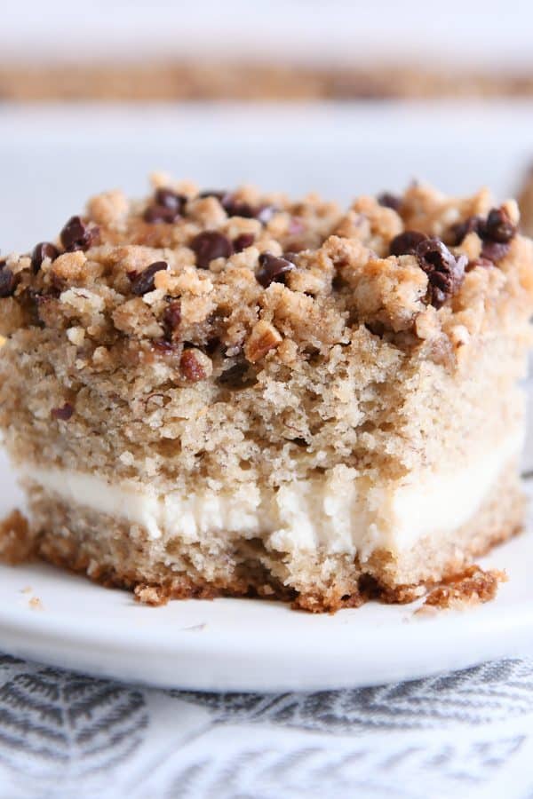 Piece of banana cream cheese coffee cake with chocolate chip streusel on white plate with bite taken out.