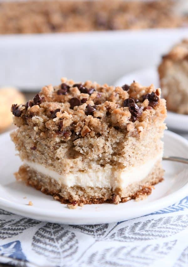 Piece of banana cream cheese coffee cake with chocolate chip streusel on white plate with bite taken out.