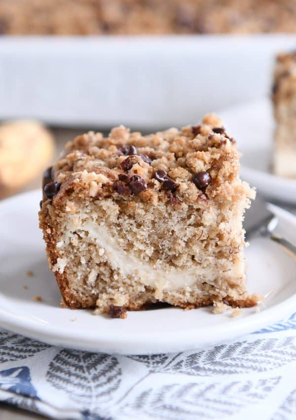 Piece of banana cream cheese coffee cake with chocolate chip streusel on white plate.
