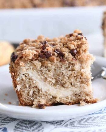 Piece of banana cream cheese coffee cake with chocolate chip streusel on white plate.